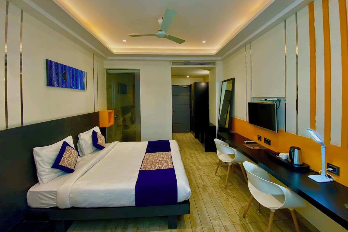 A modern hotel room with a large bed, a desk, a chair, a television, and a ceiling fan.