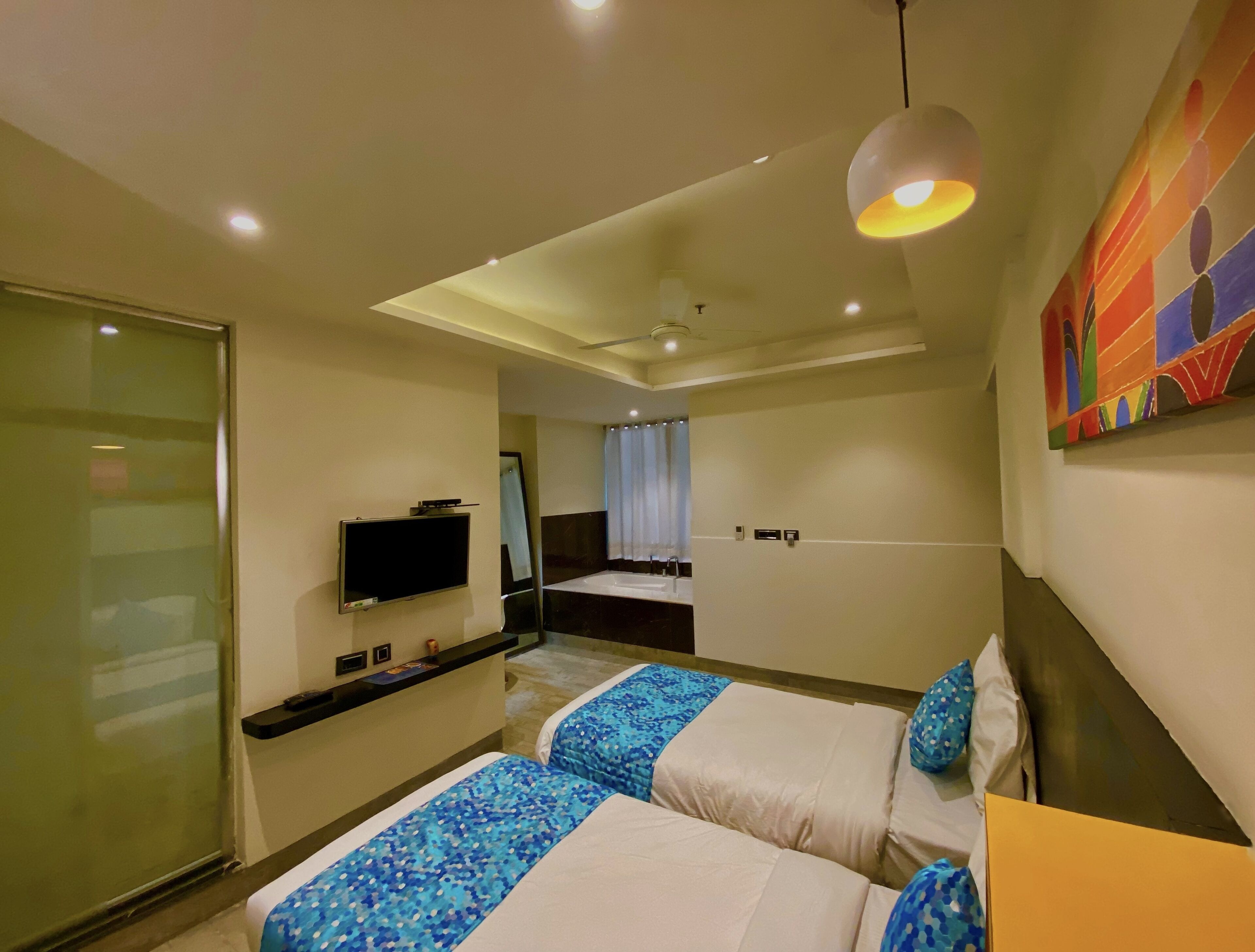 A hotel room with two beds, a TV, a bathroom, and a colorful painting on the wall.