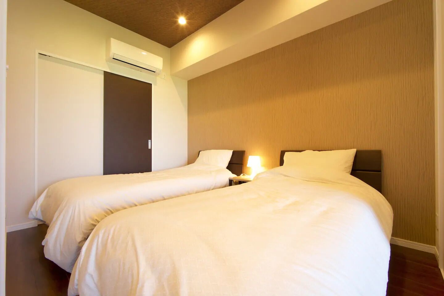Une chambre d’hôtel avec deux lits, un mur décoratif en bois et un luminaire au plafond.