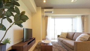 A modern living room with a flat-screen TV, a wooden coffee table, a beige sofa, and a large potted plant. - Longvacation Okinawa 209 (Onna)