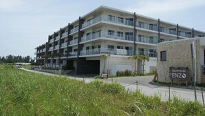 A multi-story building with balconies, a parking area, and a sign for 'pizzeria da ENZO'. - Longvacation Okinawa 209 (Onna)