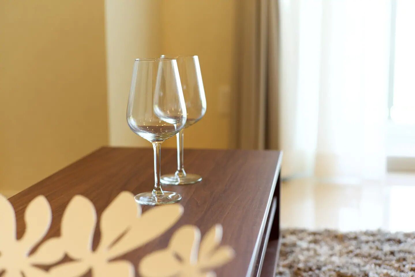 Two empty wine glasses on a wooden table with a decorative leaf pattern.