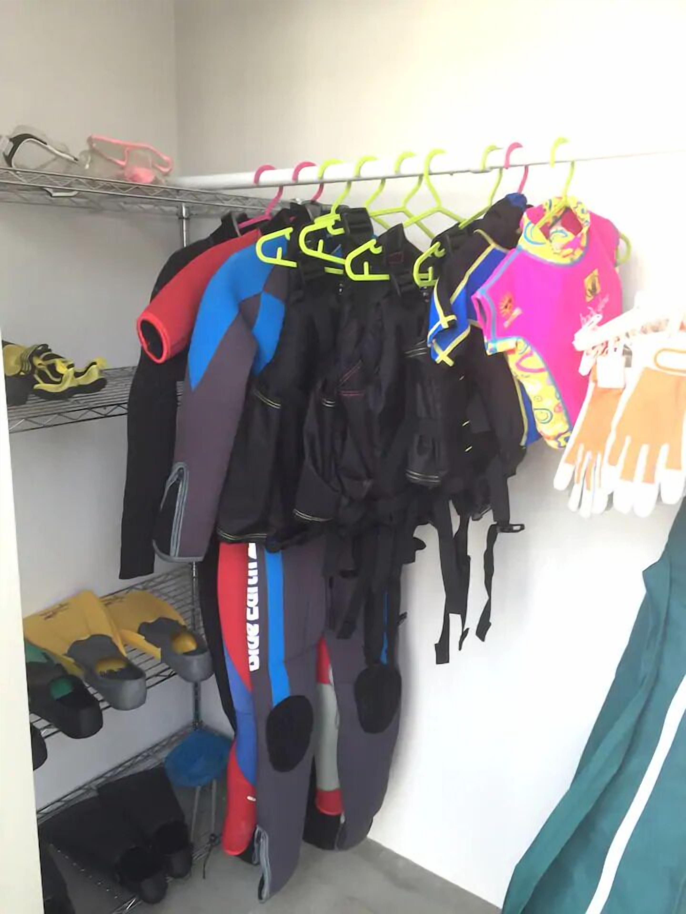 A closet with various sports gear, including shoes and wetsuits, organized on shelves and hangers.