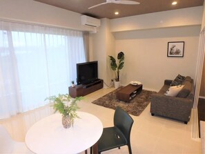 A modern living room with a flat-screen TV, a sofa, a coffee table, and a dining table with chairs. - Longvacation Okinawa 210 (Onna)
