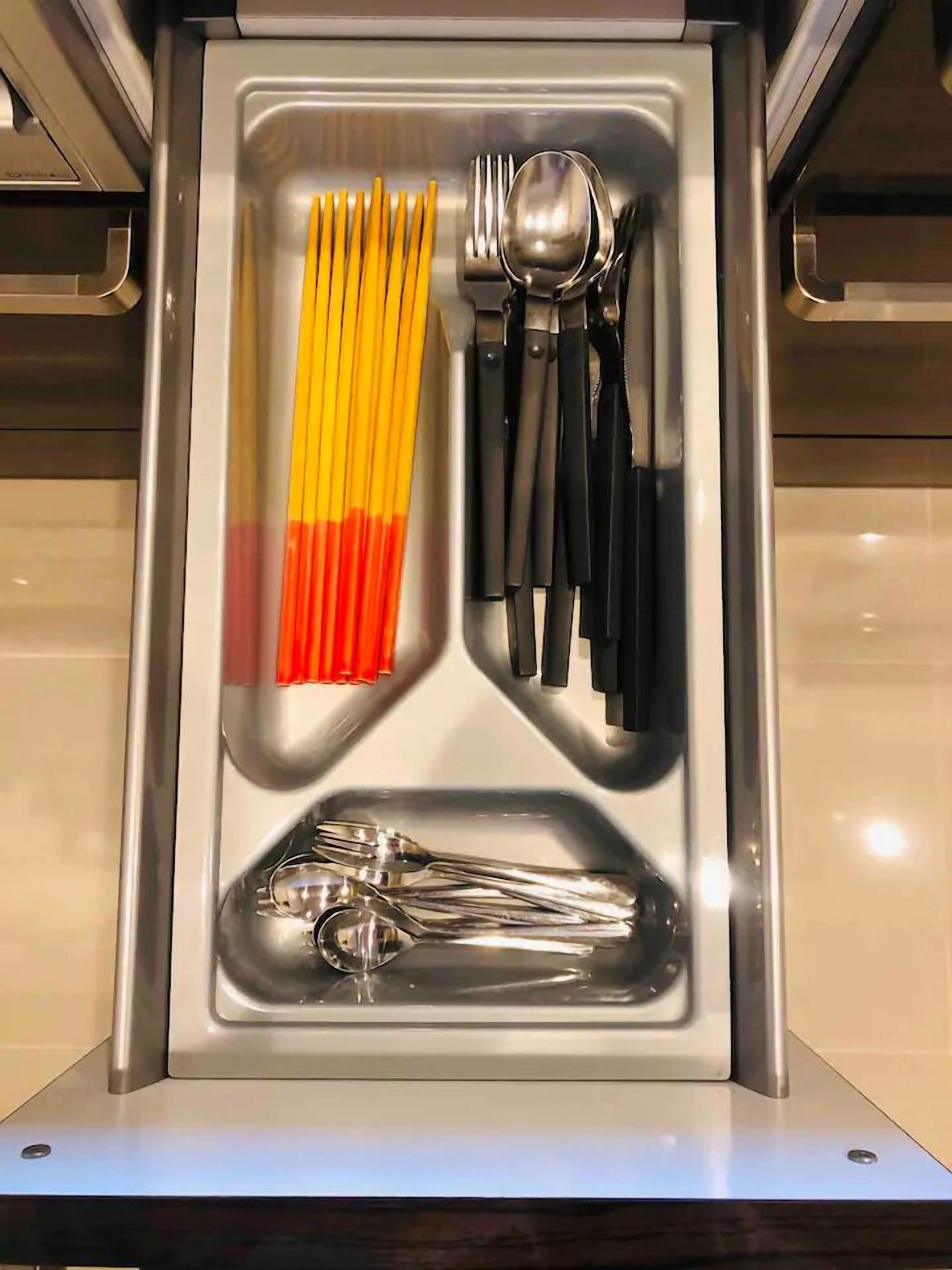 A drawer with utensils including chopsticks, forks, spoons, and tongs.