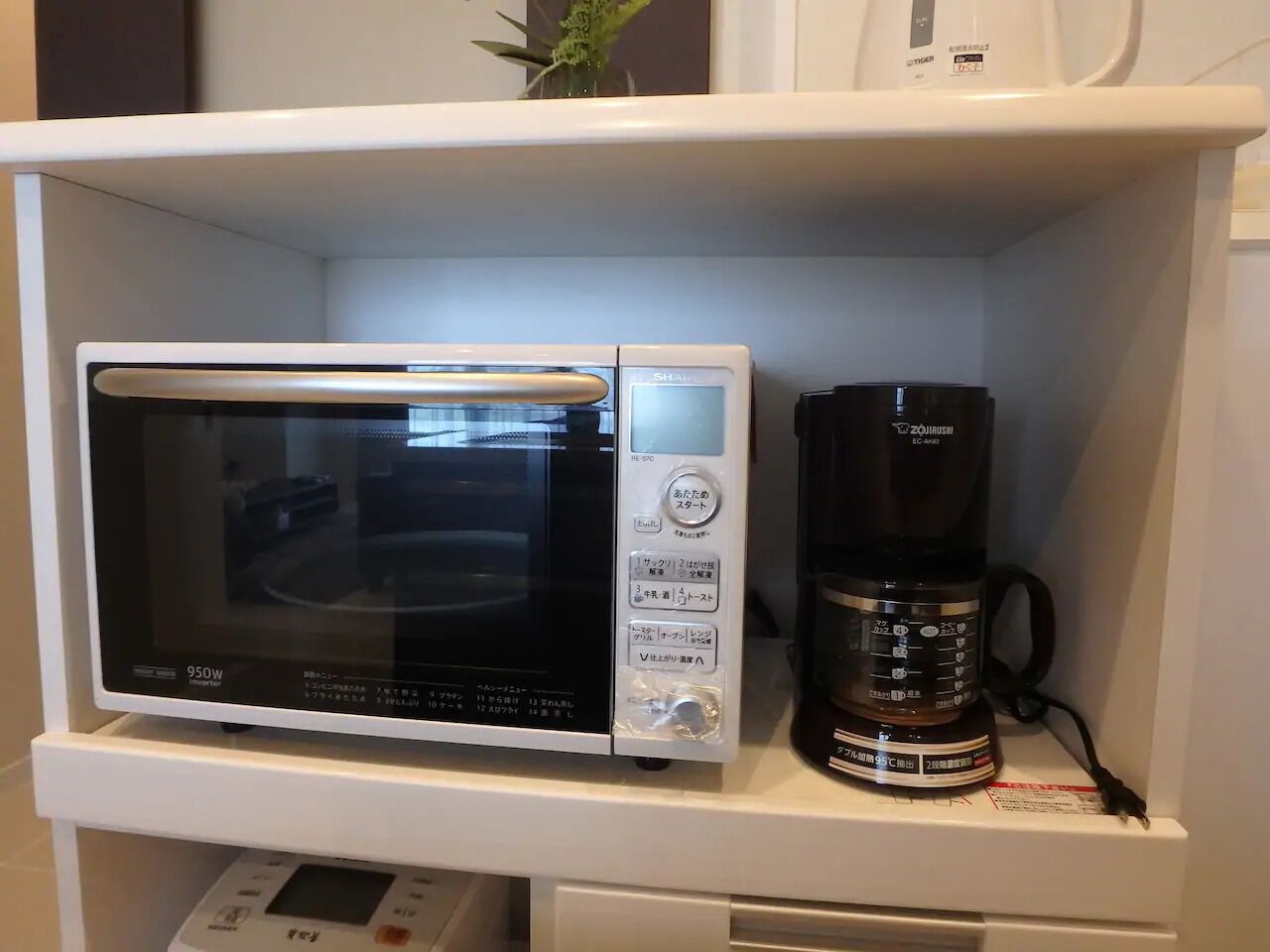 Een magnetron en een koffiezetapparaat staan op een wit schap.