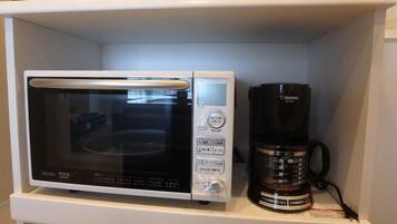 Een magnetron en een koffiezetapparaat staan op een wit schap.