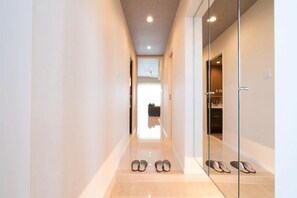 Um corredor com porta de vidro que dá para um banheiro, um par de sapatos no chão e uma luminária no teto.