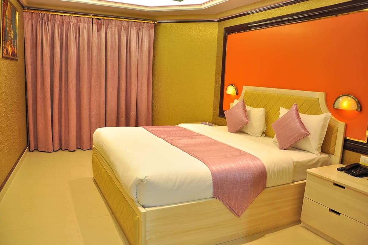 A hotel room with a large bed, a nightstand, and a wall-mounted lamp.