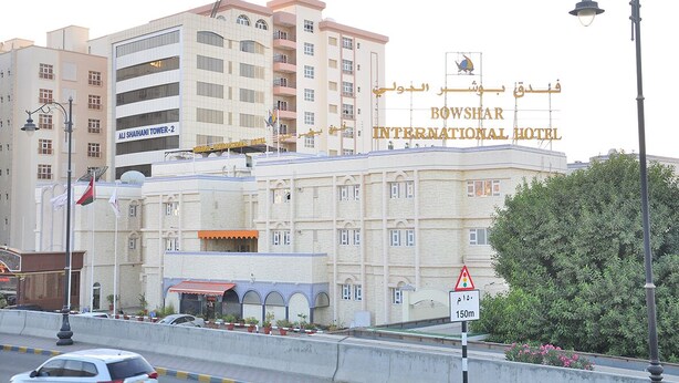 The Bowsher International Hotel with a prominent sign, a multi-story building, and a street view with cars and a traffic sign indicating a height restriction. - Bowshar International Hotel (Muscat)