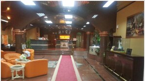 A hotel lobby with a red carpet, orange seating, a reception desk, and a large chandelier. - Bowshar International Hotel (Muscat)