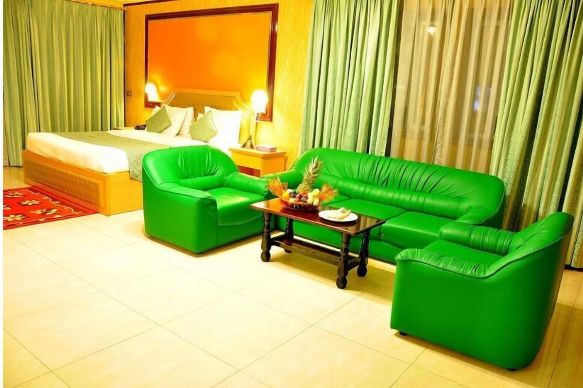 A hotel room with a bed, green leather sofa, a small table with fruit, and curtains.