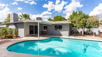 Una casa moderna con piscina, patio cubierto y jardín.