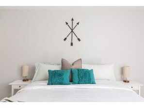 A neatly made bed with white bedding and two teal pillows, flanked by two bedside tables with lamps. - ELM - Modern 4BD / Private Pool & Walk to Biltmore (Phoenix)