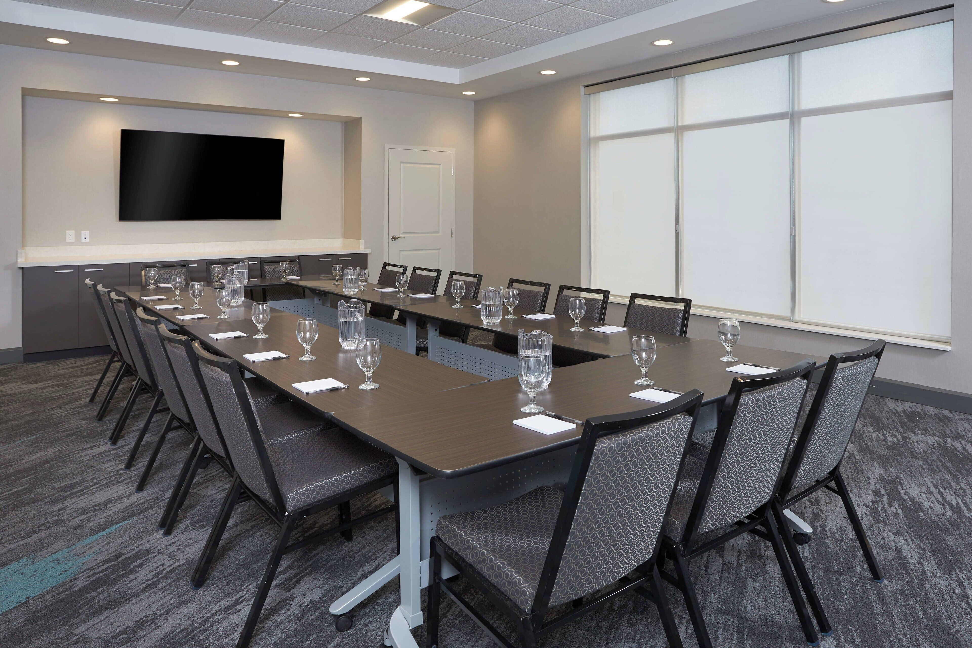 Een vergaderzaal met een lange tafel, stoelen, een televisiescherm en een projectiescherm.