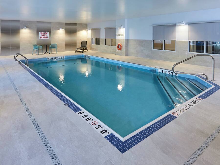 An indoor swimming pool with a shallow area marked, a lifebuoy, and a no diving sign.