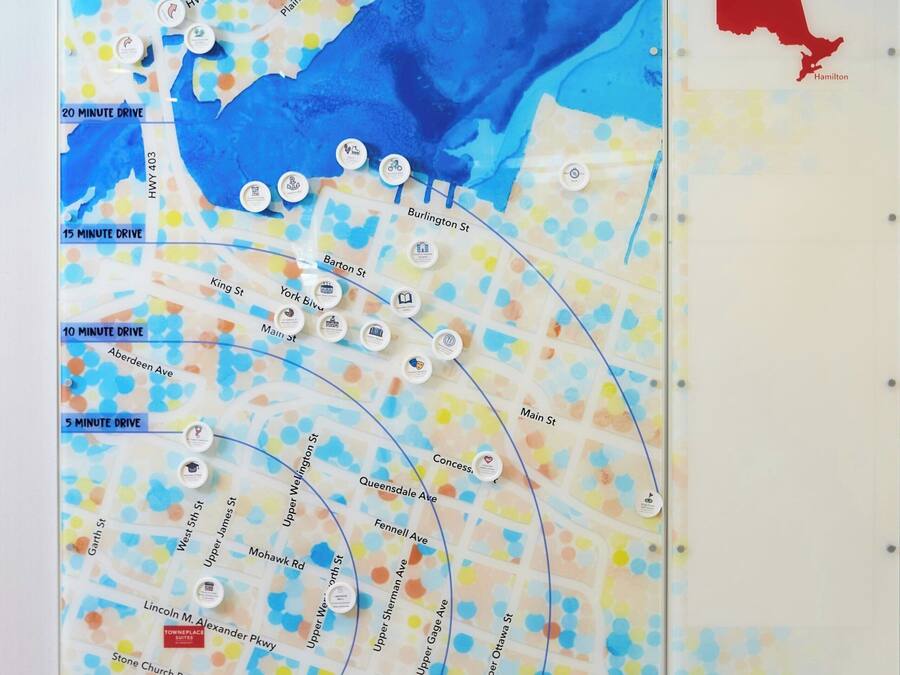 A map with various streets and drive times, a welcome sign for Hamilton, ON, and a red outline of the city.