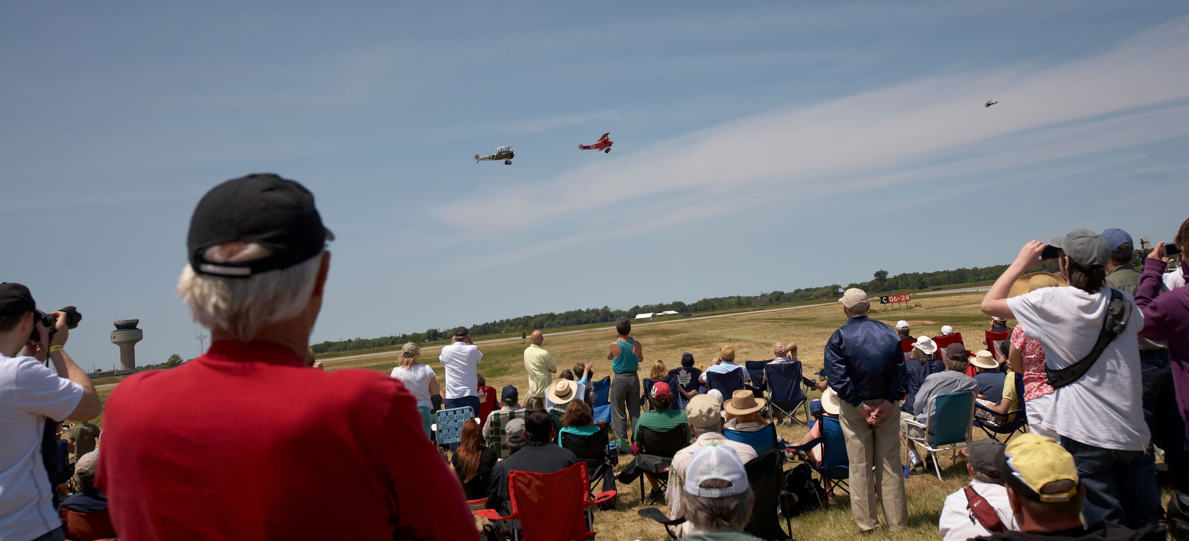 A crowd of people watching an airshow with aircraft flying overhead.
