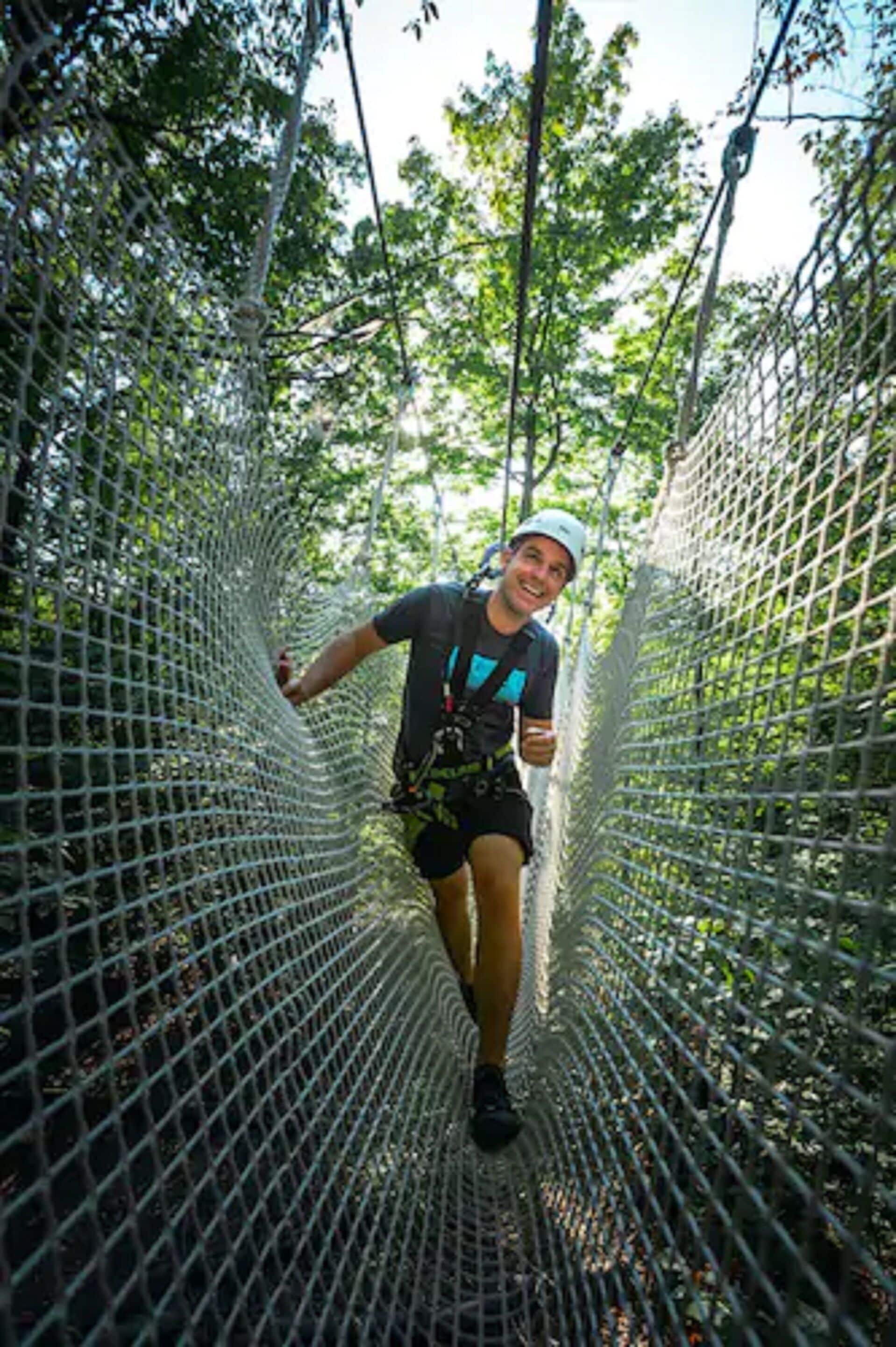 Una persona cruzando un puente colgante en un área boscosa.