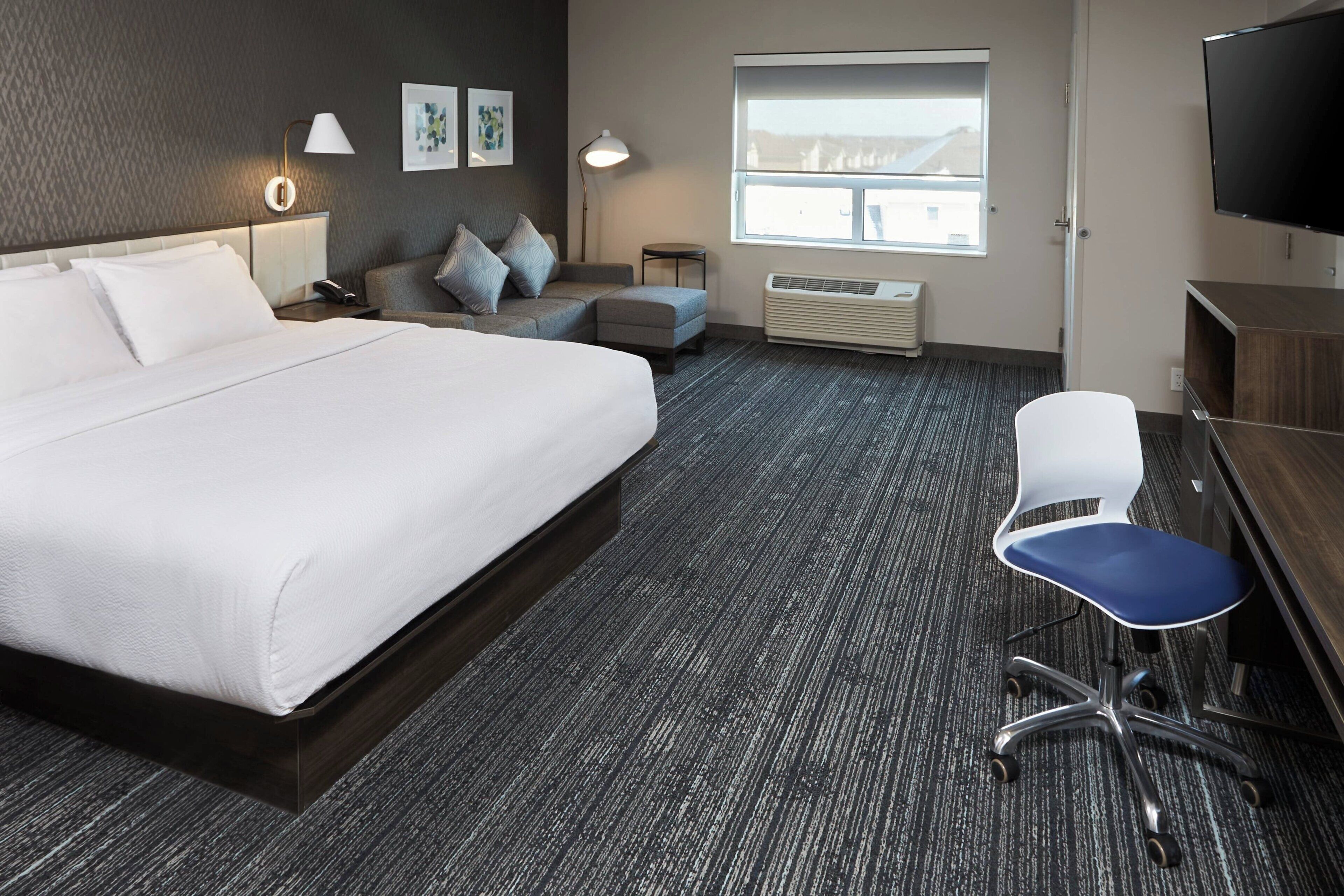 A hotel room with a large bed, a desk with a chair, a TV, and a window with a view.