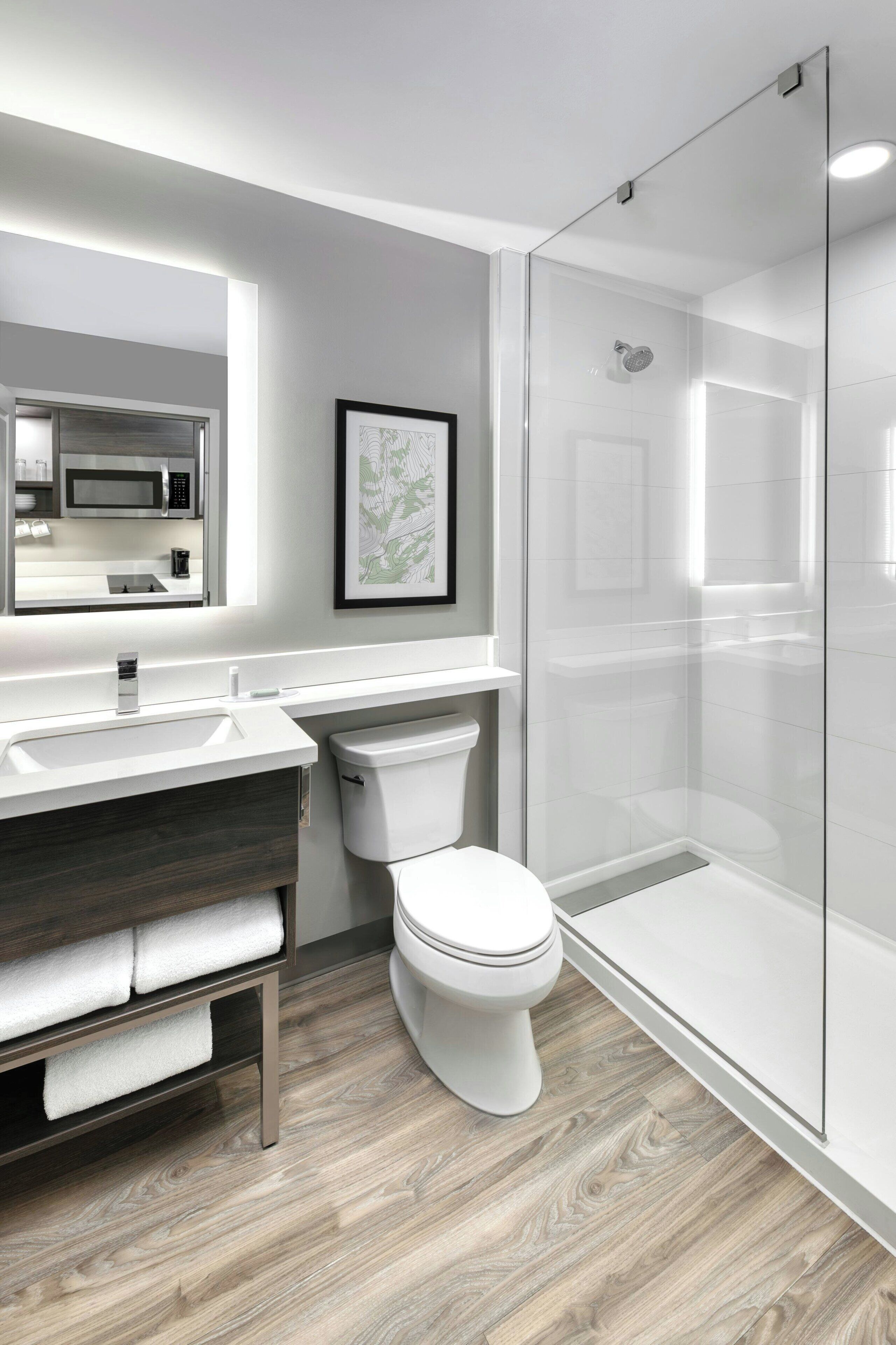 A modern bathroom with a glass shower enclosure, a white toilet, a wooden vanity, and a large mirror.