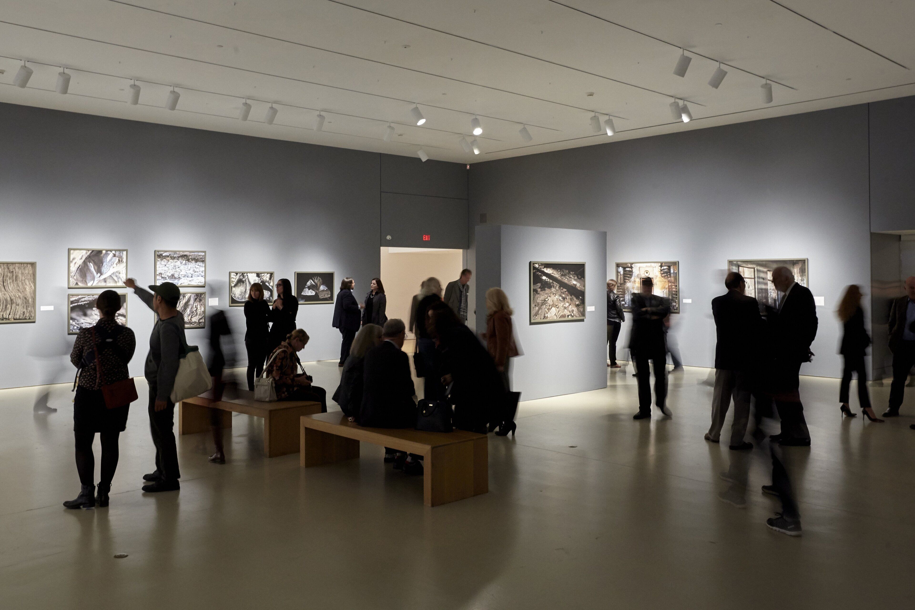 An art gallery with visitors observing artworks on the walls.