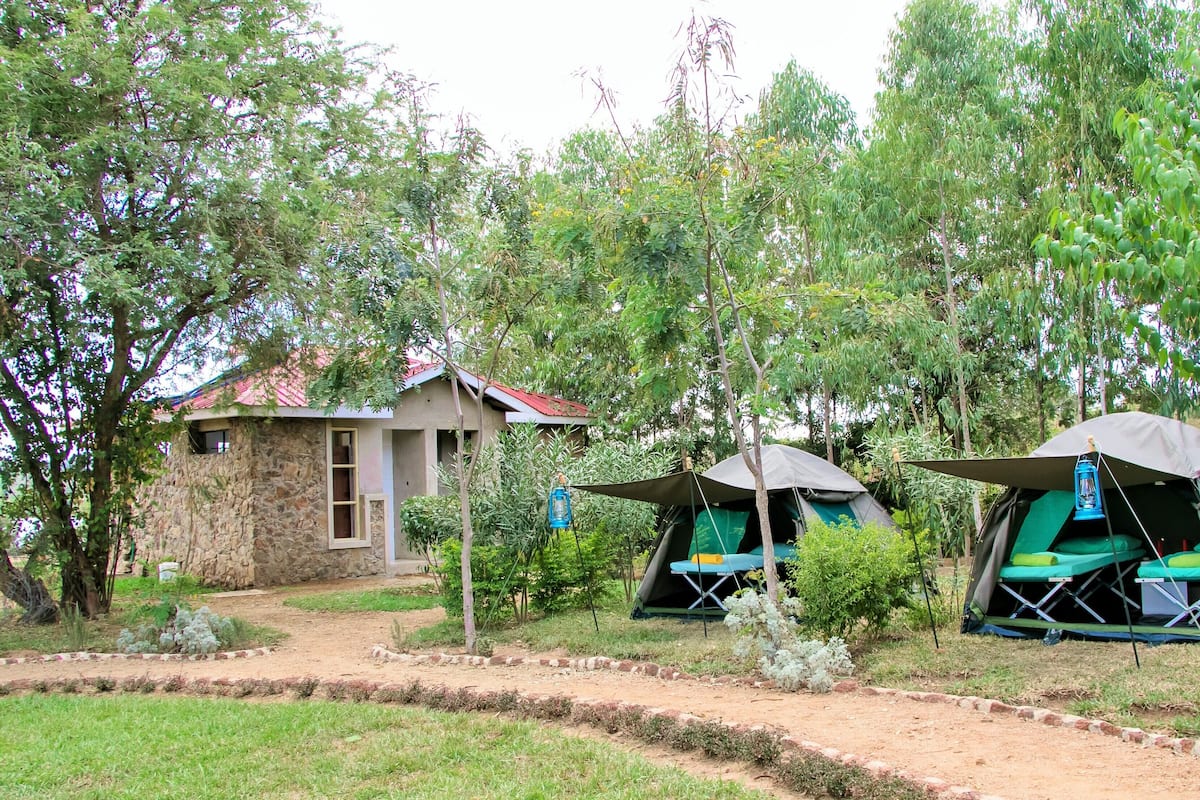 Um camping com duas tendas, um edifício de pedra e uma trilha de terra.