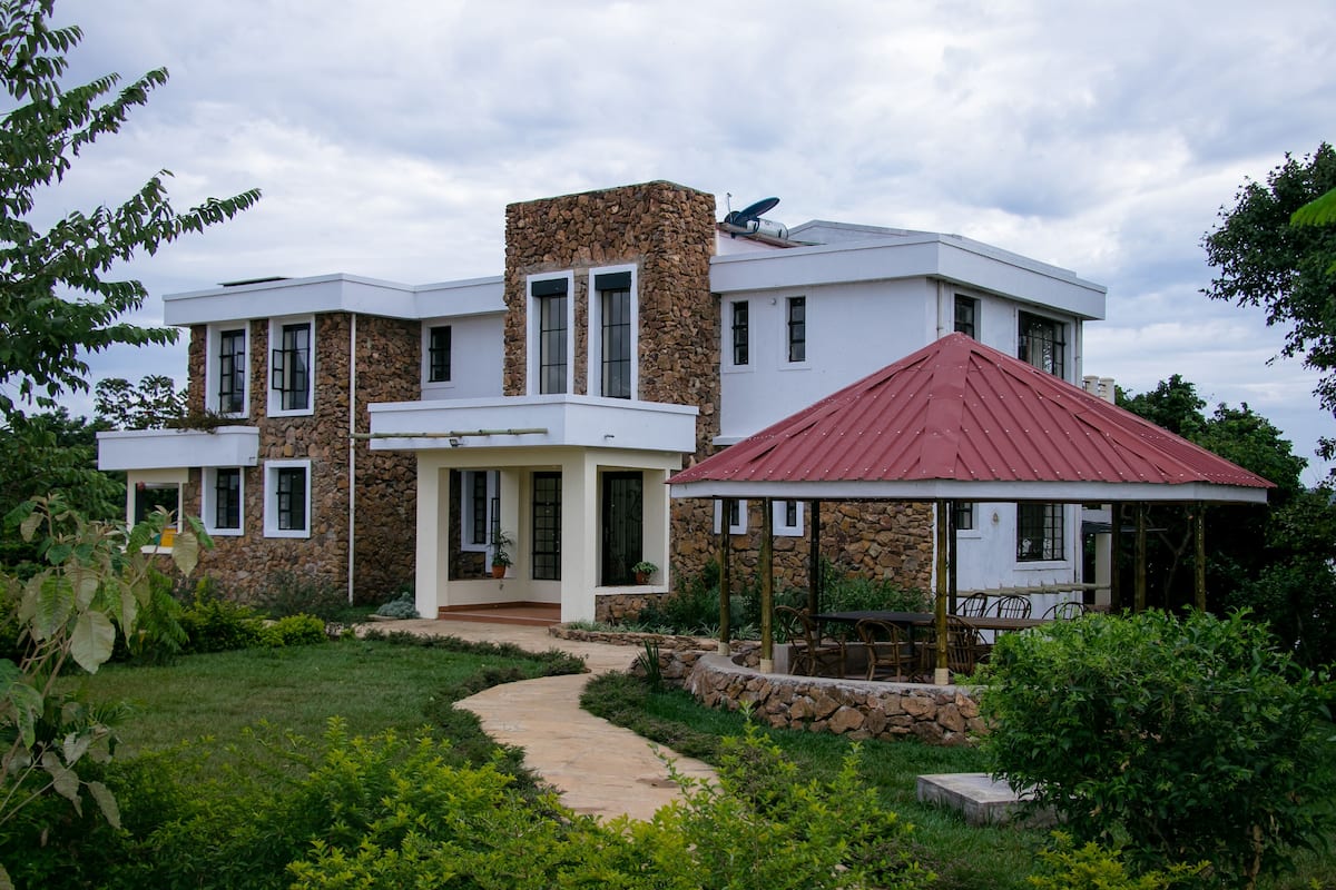 Uma casa moderna de dois andares com fachada de pedra, um gazebo com telhado vermelho e um caminho de jardim pavimentado.