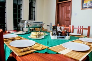 A dining table set with plates, a fruit bowl, and a buffet station. - Pikidi Gardens (Bondo)