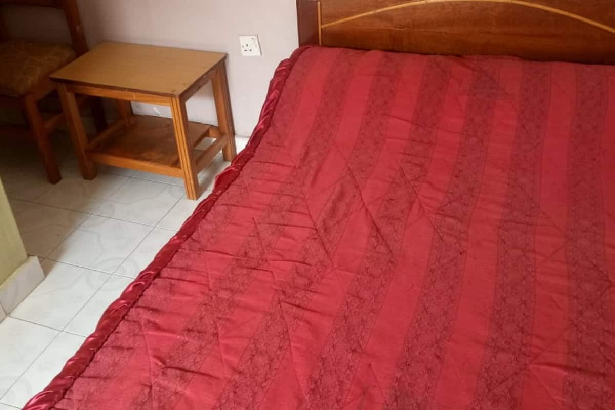 A bed with a red quilt, a wooden headboard, and a small wooden table beside it.