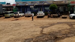 A parking lot with several cars and a few people. There are shops with signs like 'Safaricom' and 'Hot Blue Perk'. - Blue Perch Lodge (Gilgil)