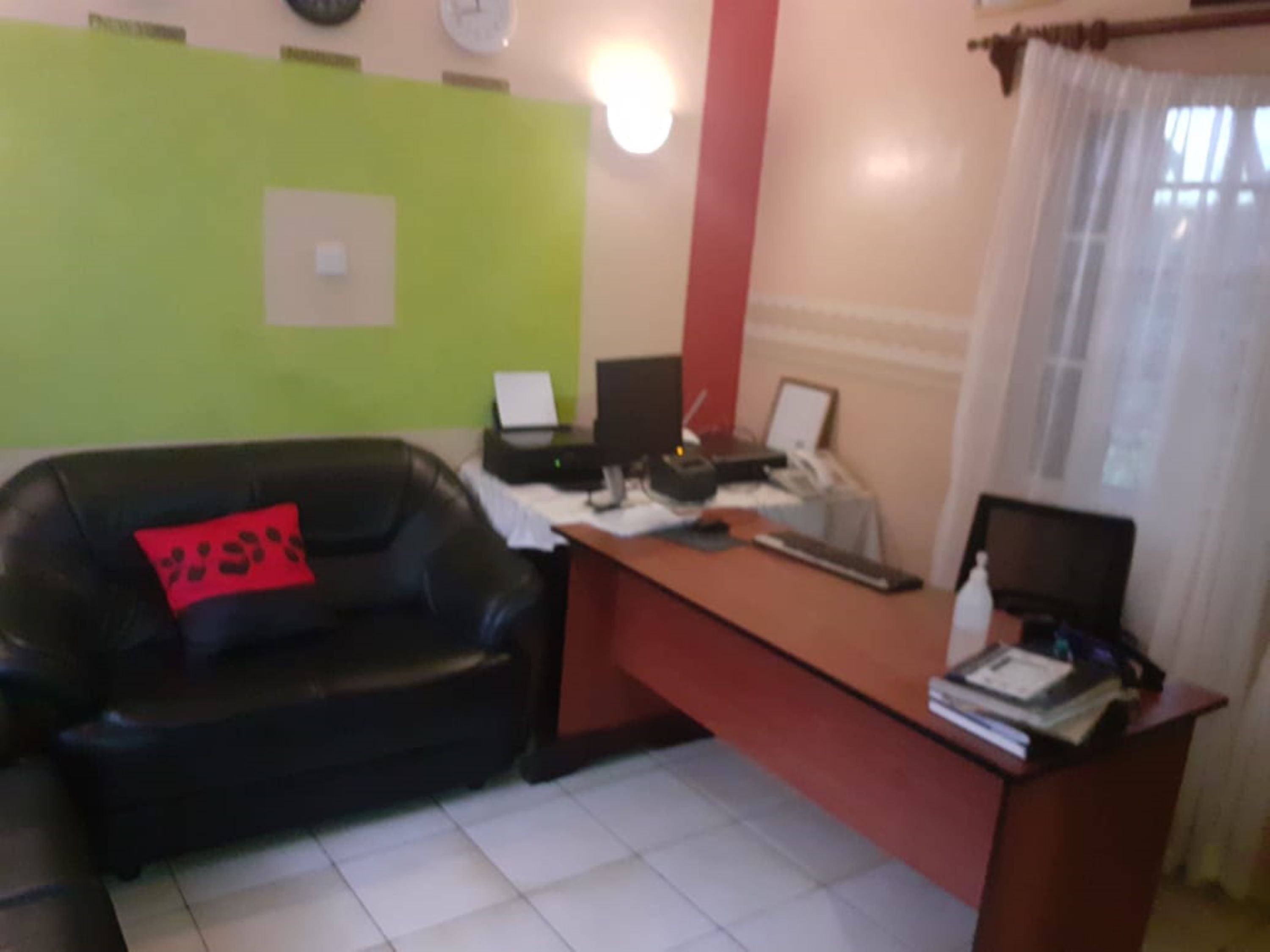 A room with a desk, a black leather couch, and a red pillow.