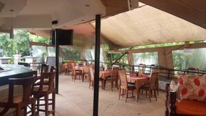 An outdoor restaurant with tables and chairs, a bar area, and a view of greenery. - Desert Rose Resort (Kisumu)