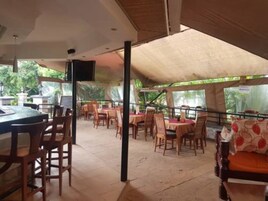 Um restaurante ao ar livre com mesas, cadeiras, um espaço de bar e vista para área verde.