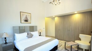 A modern hotel room with a large bed, bedside lamps, a wardrobe, a chair, and a small table. - Marbella Executive 2 Bedrooms (Dubai)