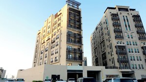 A multi-story residential building with balconies, a parking area with several cars, and a clear sky. - Marbella Executive 2 Bedrooms (Dubai)