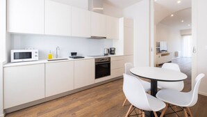 A modern kitchen with white cabinets, a microwave, a coffee maker, and a dining area with a round table and white chairs. - Casa Amarela 22 (Azores Premium at city center) (Ponta Delgada)