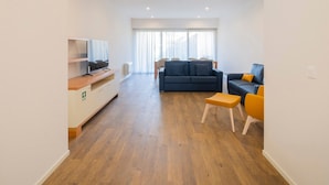 A spacious living area with a flat-screen TV, a sofa, a dining table, and a small stool. - Casa Amarela 22 (Azores Premium at city center) (Ponta Delgada)
