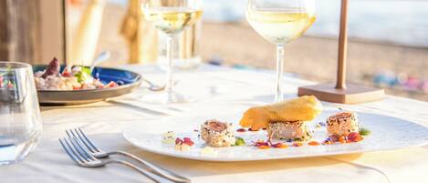 Una mesa de comedor con un plato de mariscos, copas de vino y vista a la playa.
