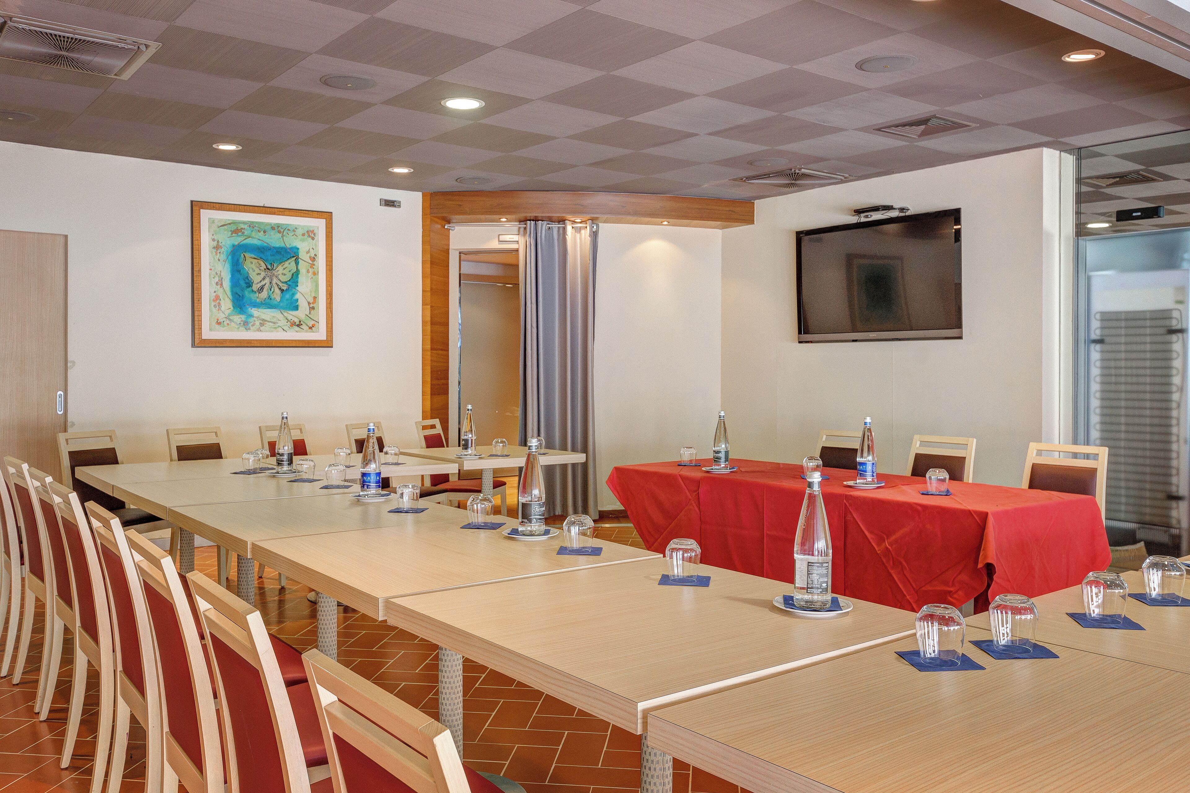 A conference room with a long table, chairs, and a red tablecloth. There are water bottles and glasses on the table.