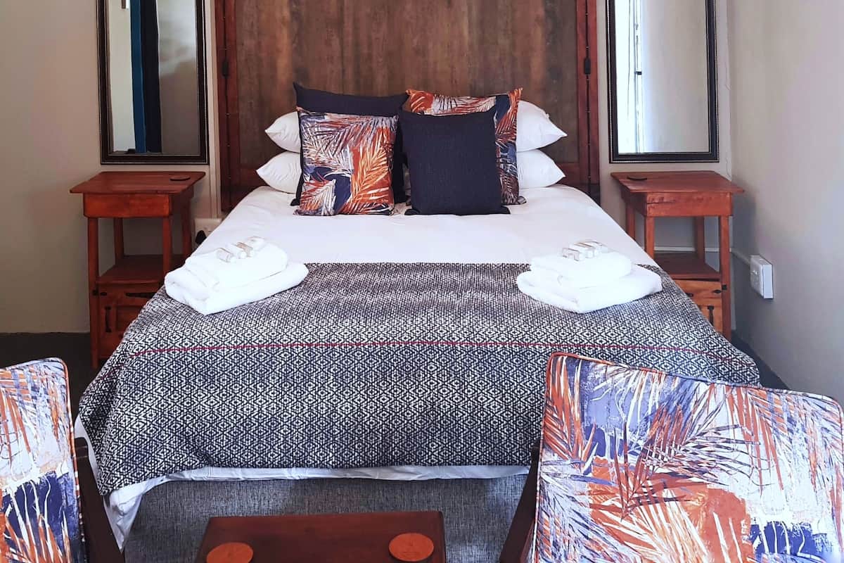 A neatly made bed with patterned bedding, two bedside tables, and a chair with a leaf-patterned cushion.