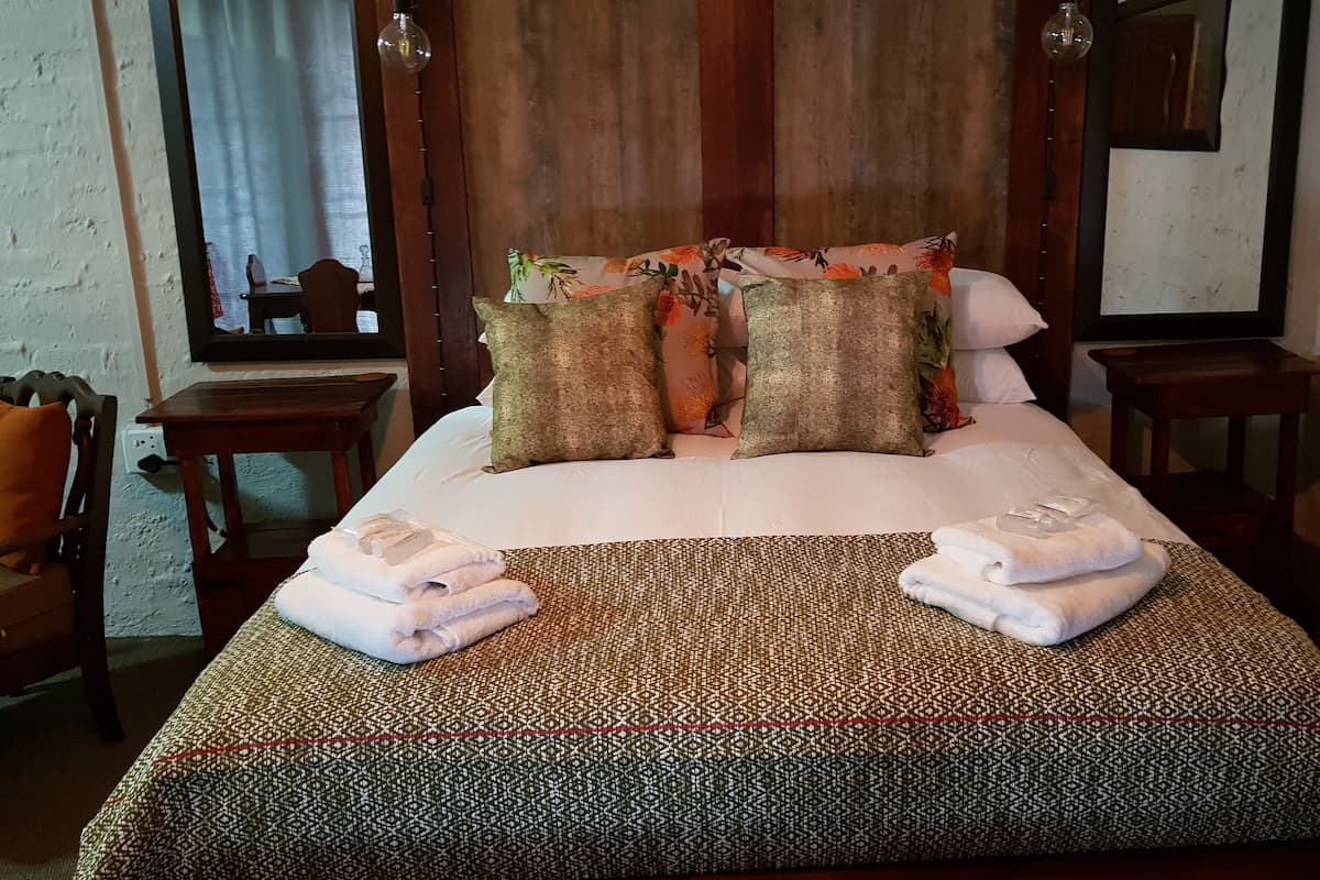 A neatly made bed with patterned bedding, two bedside tables, a chair, and a mirror on the wall.