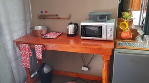 Una cocina con cubierta de madera, microondas, hervidor, pileta y refrigerador.