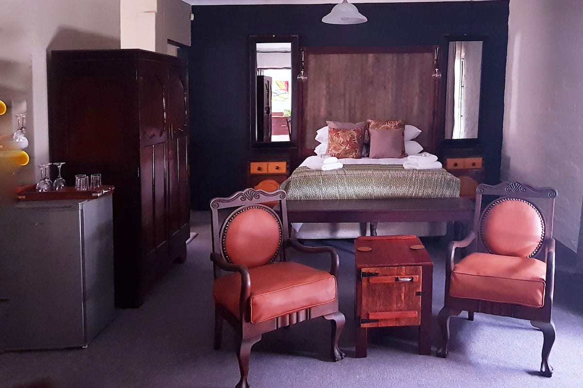 A room with a wooden bed, two upholstered chairs, a small table, and a cabinet.