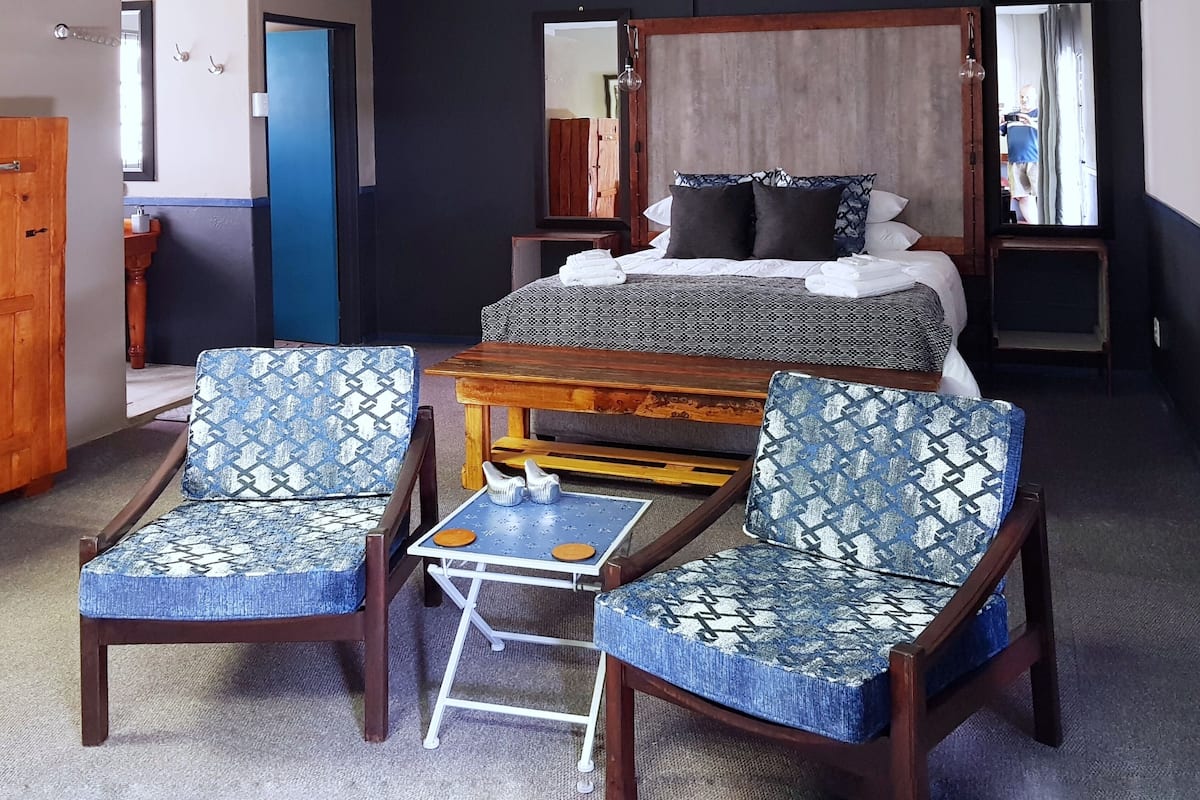 A bedroom with a bed, two patterned chairs, a small table, and a wooden wardrobe.
