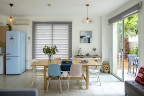A modern kitchen with a blue refrigerator, a dining table with chairs, and a large window with blinds.