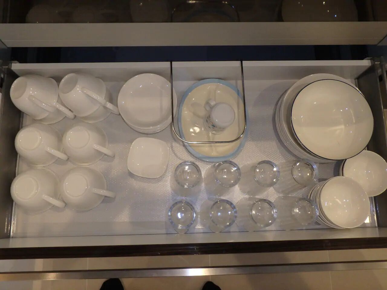 A drawer containing various white ceramic items including cups, bowls, and plates.