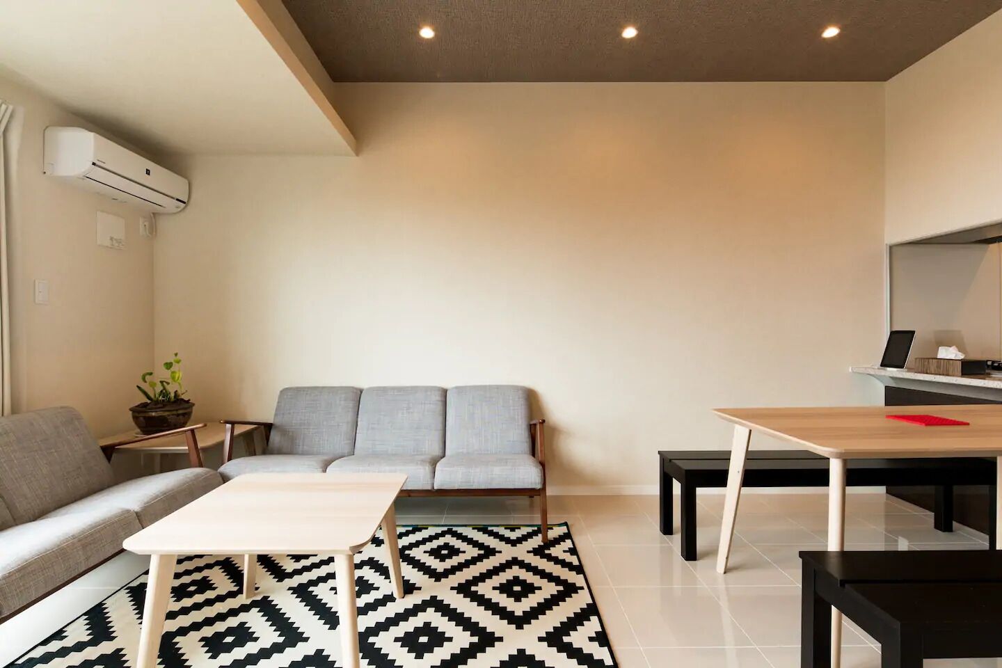 Ein modernes Wohnzimmer mit grauem Sofa, einem Holztisch, einem schwarz-weißen Teppich und einem kleinen Beistelltisch mit Pflanze.