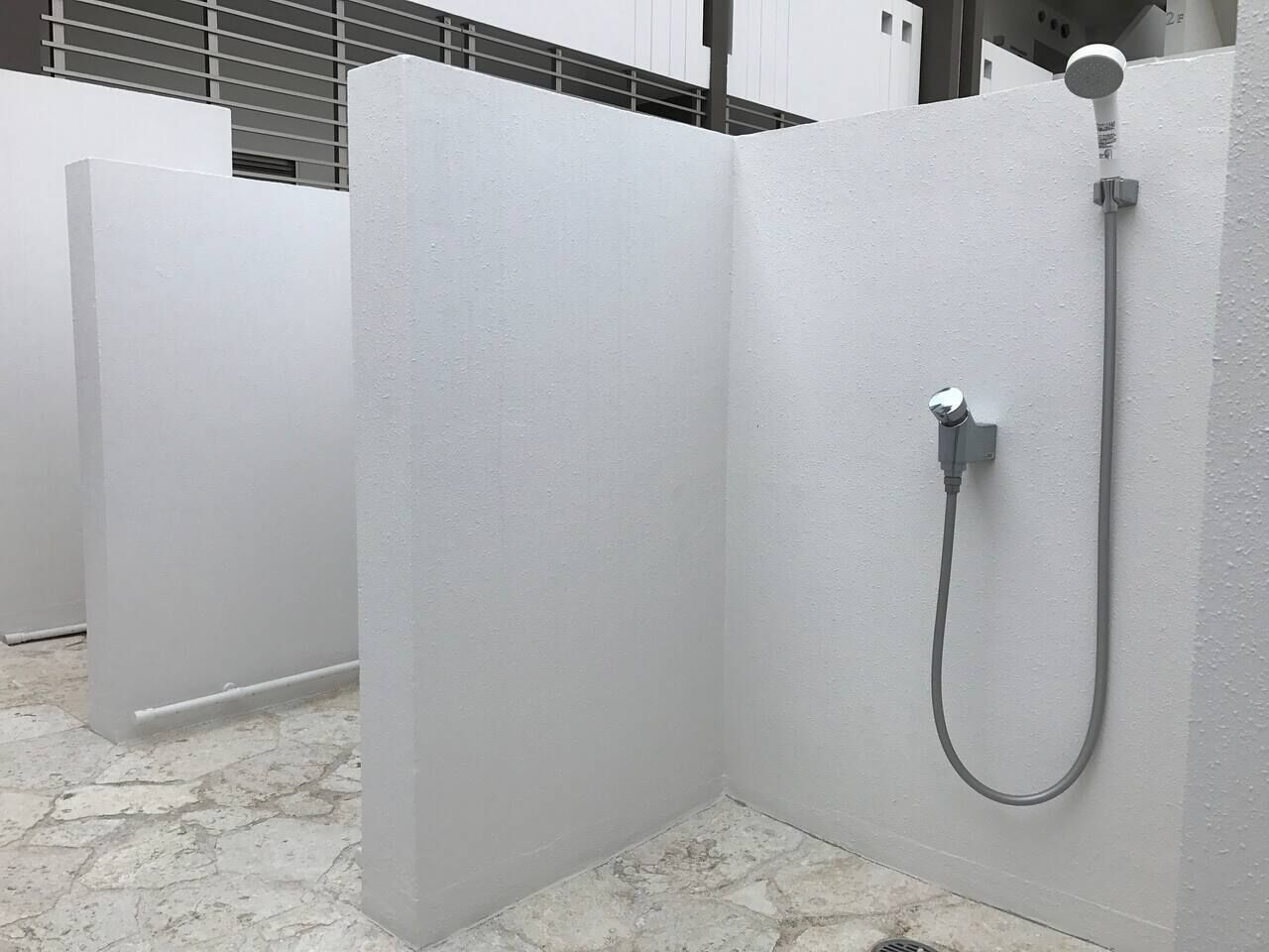 A shower enclosure with a handheld showerhead and a wall-mounted control valve.