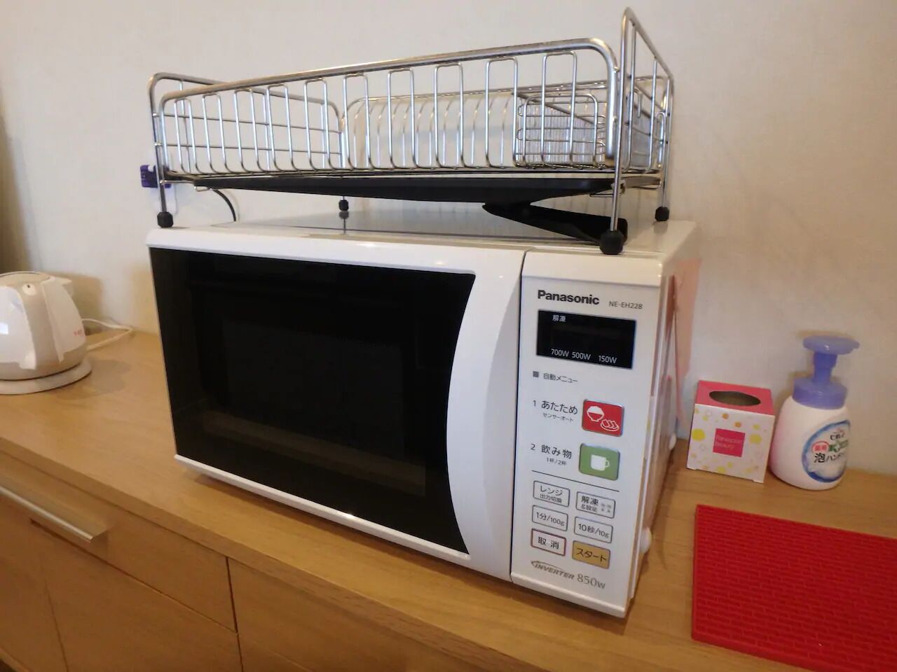 Un microondas Panasonic con pantalla digital, dispensador de agua y un caja de pañuelos sobre una encimera de madera.